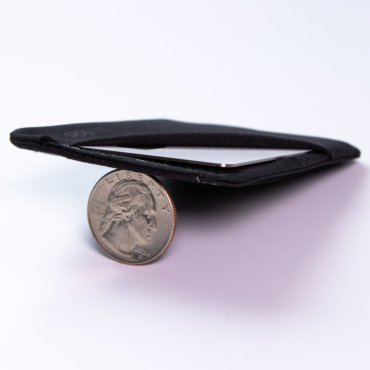 A black fabric minimalist wallet shown on a white background with a US quarter coin in front for scale. all-groups