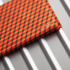 A slimfold wallet with a orange and black 3D optical illusion pattern, resting on a metallic silver ribbed surface. The brand name 'slimfold' is visible on the bottom right corner.