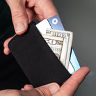 A close-up of a black fabric minimalist card holder wallet being held in two hands, with a U.S. all-groups